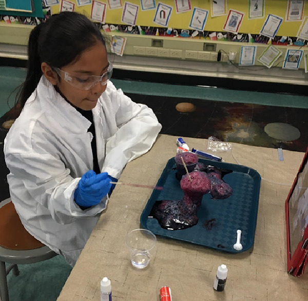 Student watches pink foam spill out of a cup