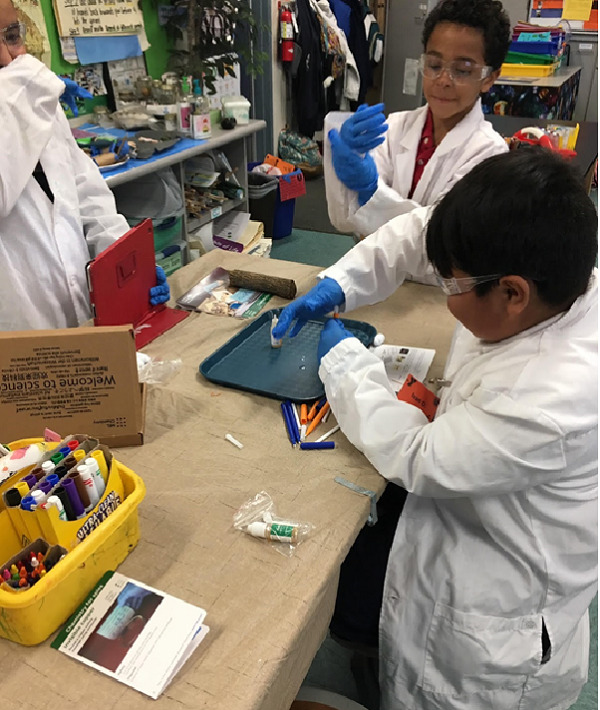 Three boys in lab coats filming and conducting an experiment