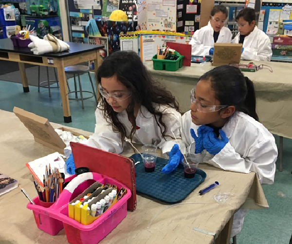 Two Girls hunched over an experiment reading the instructions